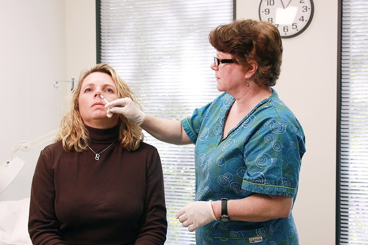 Nurse giving a nasal flu vaccine to lower risk during cold vs flu vs RSV season